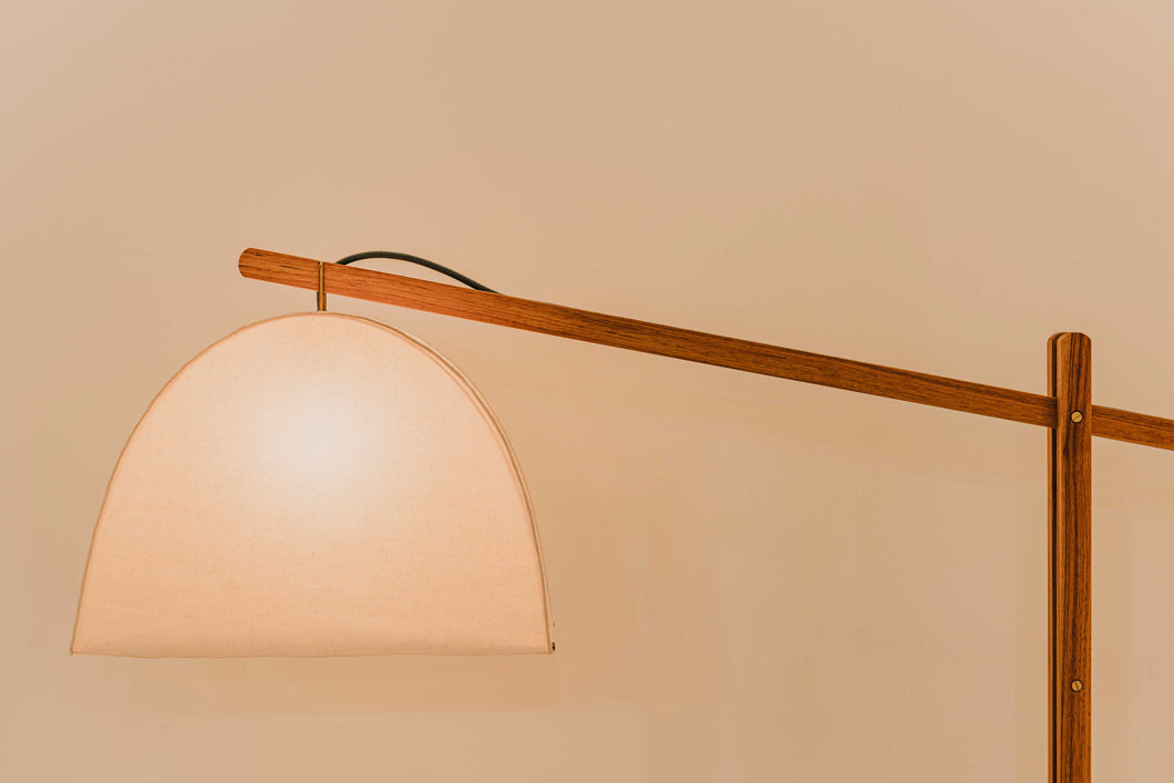 Skye Floor Lamp with illuminated natural canvas shade. American pecan wood arm extends from the base with cantilevered support, adjustable 30 degrees.